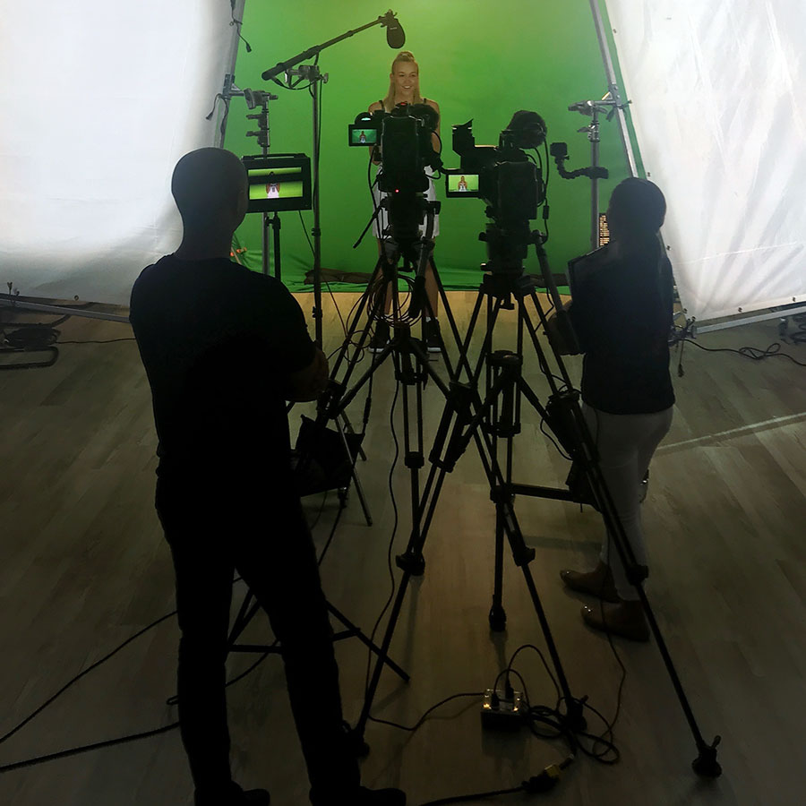 Penn State Lady Lion basketball player in the background in front of a green screen with a camera and sound crew silhouetted in the foreground.