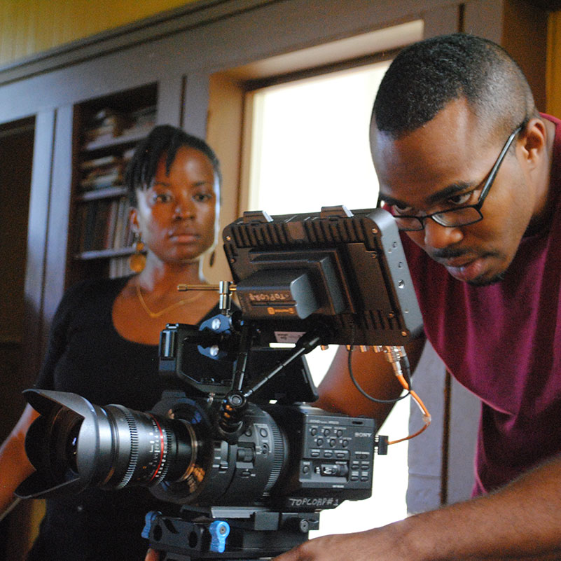 A videographer focuses on getting the shot while a producer watches from the background.