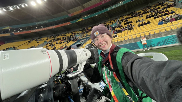 College student in a carhartt beanie cap with a long lens camera poses in an empty stadium after a world cup soccer match in New Zealand